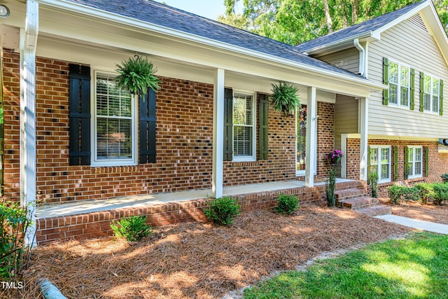 exterior space featuring covered porch, a shingled roof, and brick siding