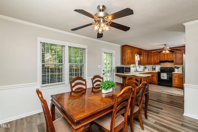 dining space with a textured ceiling, ceiling fan, ornamental molding, and light wood-style floors