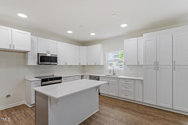 kitchen with a kitchen island, dark wood-style flooring, a sink, light countertops, and stainless steel appliances