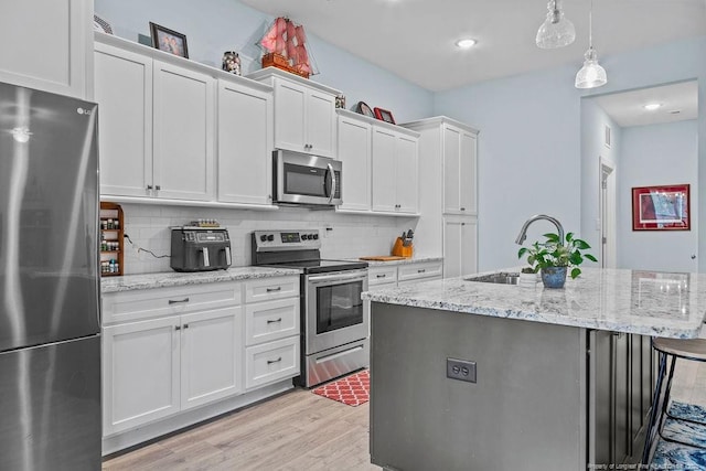 kitchen with white cabinetry, a sink, light wood-style flooring, backsplash, and stainless steel appliances