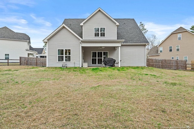 back of house featuring a lawn, a shingled roof, a ceiling fan, and a fenced backyard