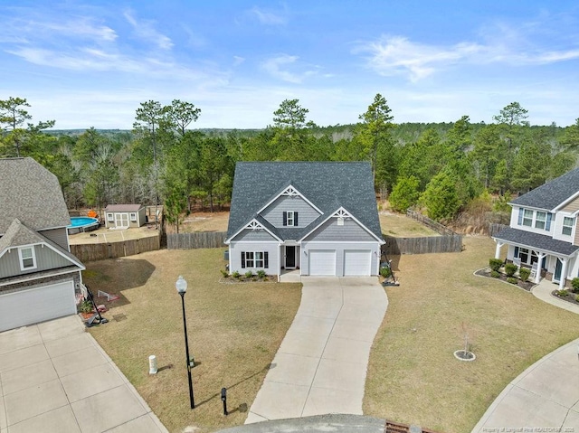 view of front of property featuring fence, driveway, a forest view, and a front lawn
