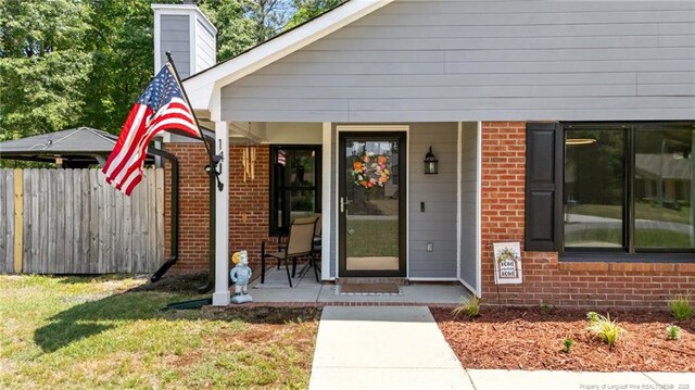 property entrance with a porch, a chimney, brick siding, fence, and a yard
