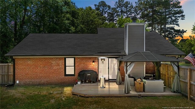 back of property at dusk featuring brick siding, a gazebo, a wooden deck, and a fenced backyard