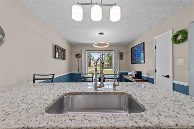 kitchen featuring a sink, a textured ceiling, decorative light fixtures, and light stone countertops