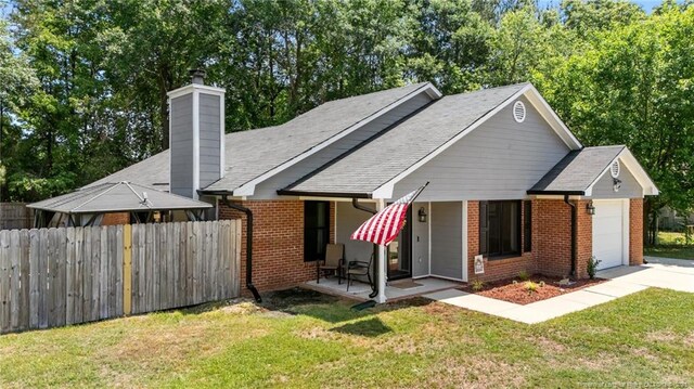 view of front of property featuring brick siding, an attached garage, fence, and a front lawn