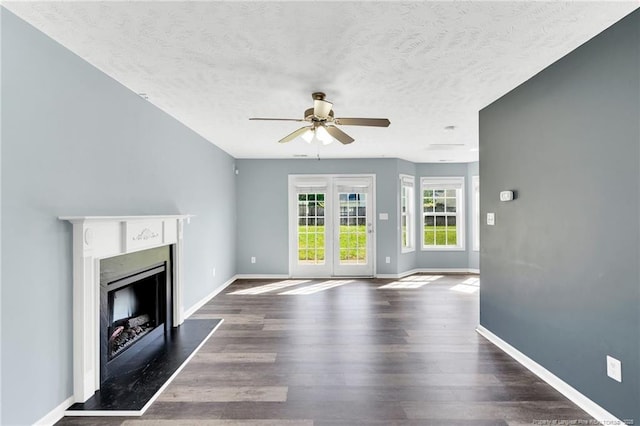 unfurnished living room featuring a fireplace, a textured ceiling, a ceiling fan, baseboards, and dark wood-type flooring