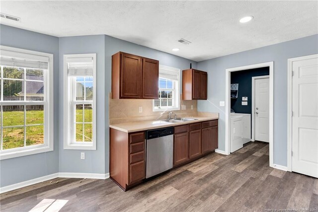 kitchen featuring washing machine and clothes dryer, a sink, dishwasher, baseboards, and dark wood-type flooring