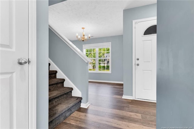 entryway with a textured ceiling, a chandelier, baseboards, wood finished floors, and stairway