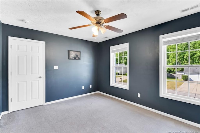 carpeted spare room with visible vents, baseboards, and ceiling fan