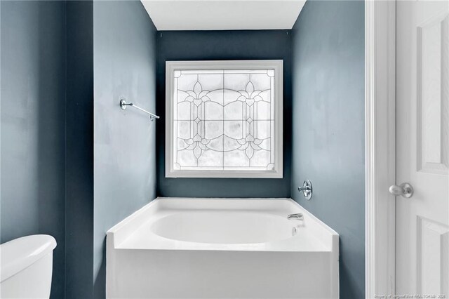 bathroom featuring a garden tub and toilet