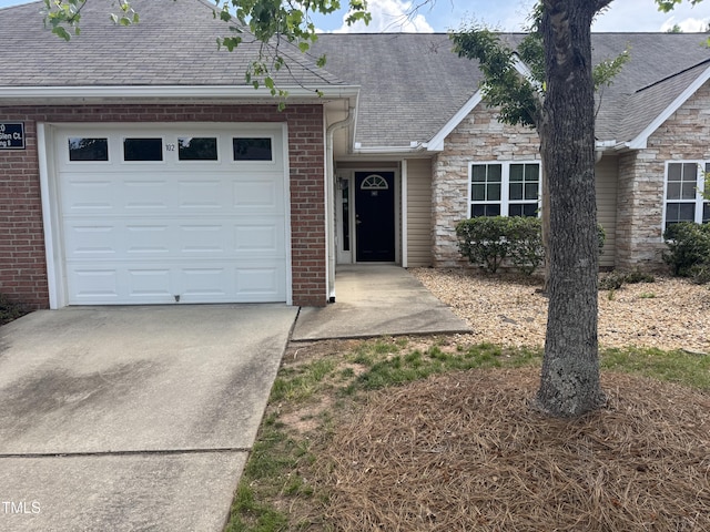 ranch-style house with concrete driveway, brick siding, a shingled roof, and a garage