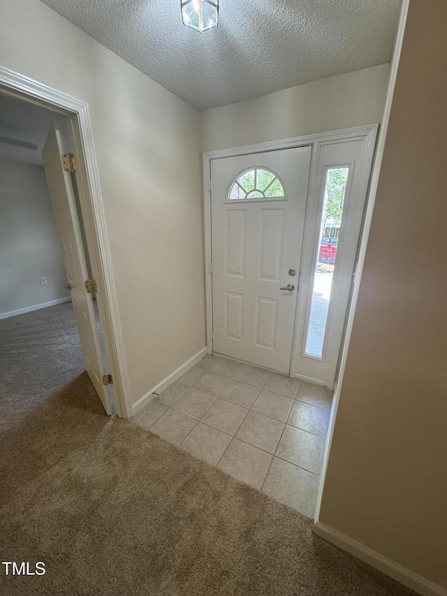 foyer entrance with baseboards, a textured ceiling, light tile patterned floors, and light colored carpet