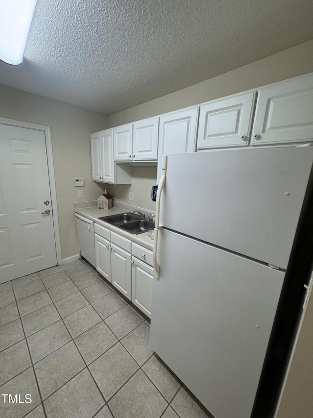 kitchen with a textured ceiling, light tile patterned floors, a sink, white cabinets, and white appliances