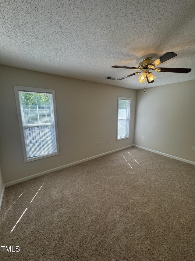 carpeted empty room with baseboards, ceiling fan, a textured ceiling, and visible vents