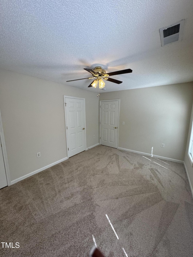 empty room featuring visible vents, carpet floors, baseboards, a textured ceiling, and a ceiling fan