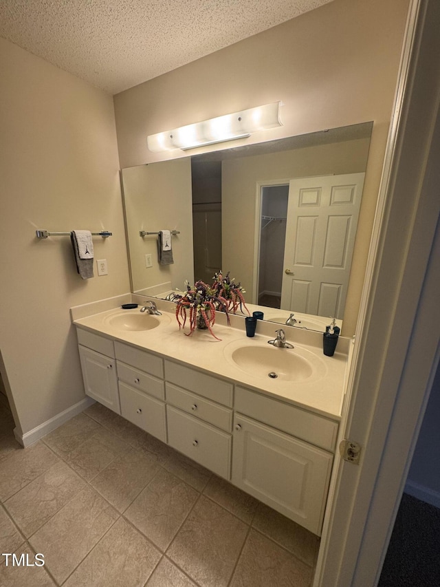 bathroom featuring a sink, a textured ceiling, baseboards, and double vanity
