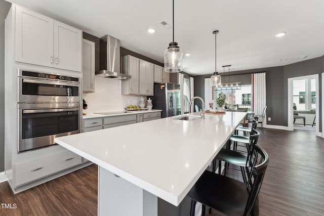kitchen with light countertops, stainless steel appliances, a sink, and wall chimney exhaust hood