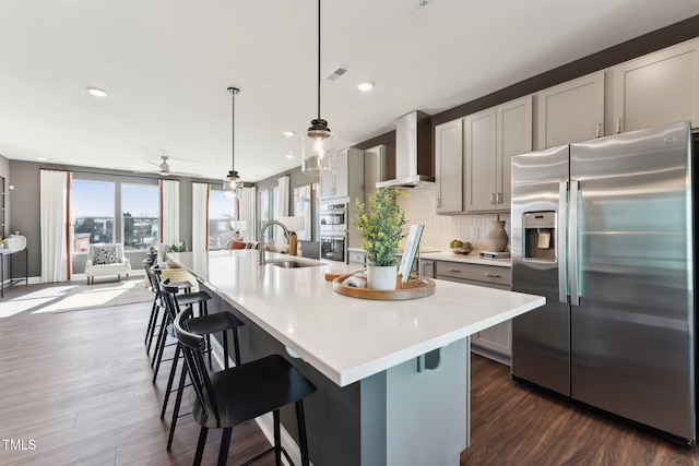 kitchen with a sink, light countertops, stainless steel appliances, wall chimney exhaust hood, and dark wood-type flooring