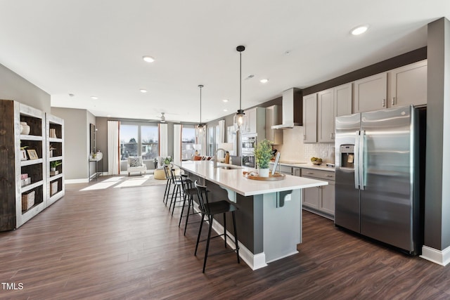 kitchen featuring wall chimney range hood, dark wood finished floors, light countertops, stainless steel fridge with ice dispenser, and a breakfast bar