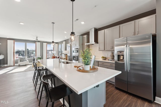 kitchen featuring a sink, light countertops, wall chimney exhaust hood, stainless steel appliances, and backsplash