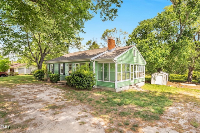 2677 NC-39, Henderson, NC 27537 - view of side of home featuring a storage unit, a shingled roof, a sunroom, an outbuilding, and a chimney