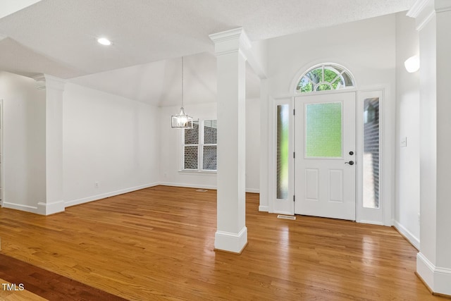 entrance foyer featuring light wood finished floors, a textured ceiling, baseboards, lofted ceiling, and ornate columns