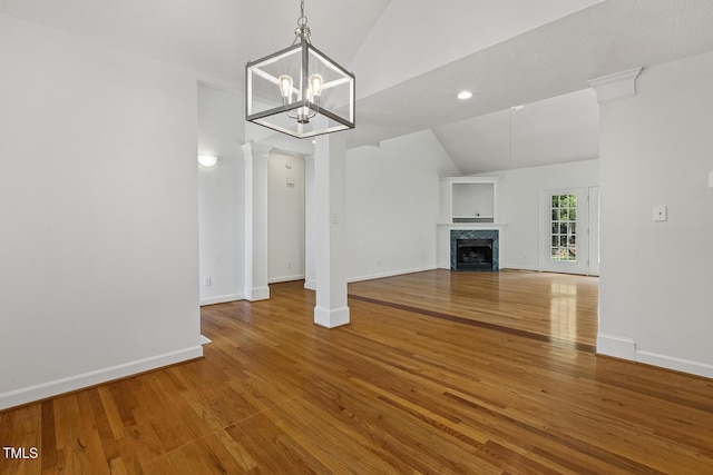 unfurnished living room featuring an inviting chandelier, wood finished floors, lofted ceiling, a fireplace, and baseboards