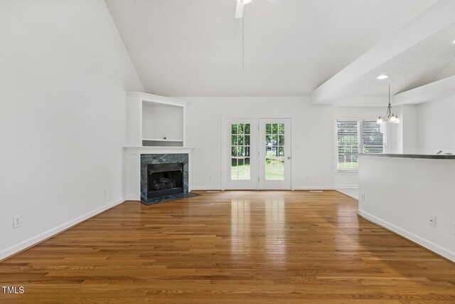 unfurnished living room with a high end fireplace, baseboards, ceiling fan with notable chandelier, and wood finished floors