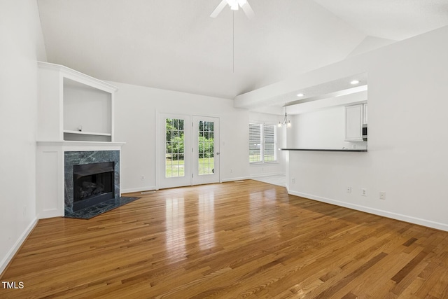 unfurnished living room with a high end fireplace, wood finished floors, baseboards, ceiling fan with notable chandelier, and lofted ceiling