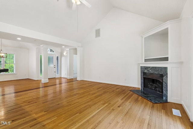 unfurnished living room with a ceiling fan, visible vents, a high end fireplace, light wood-type flooring, and high vaulted ceiling