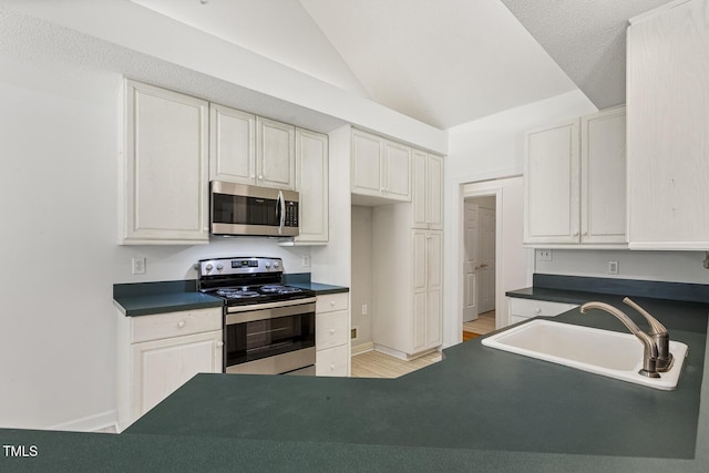 kitchen featuring appliances with stainless steel finishes, dark countertops, vaulted ceiling, light wood-type flooring, and a sink