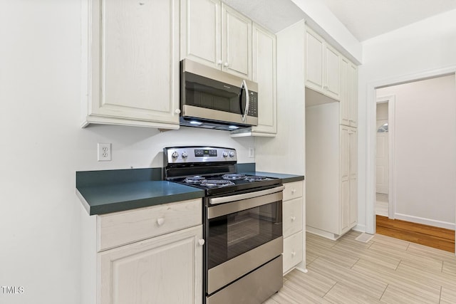 kitchen featuring stainless steel appliances, dark countertops, baseboards, and light wood finished floors