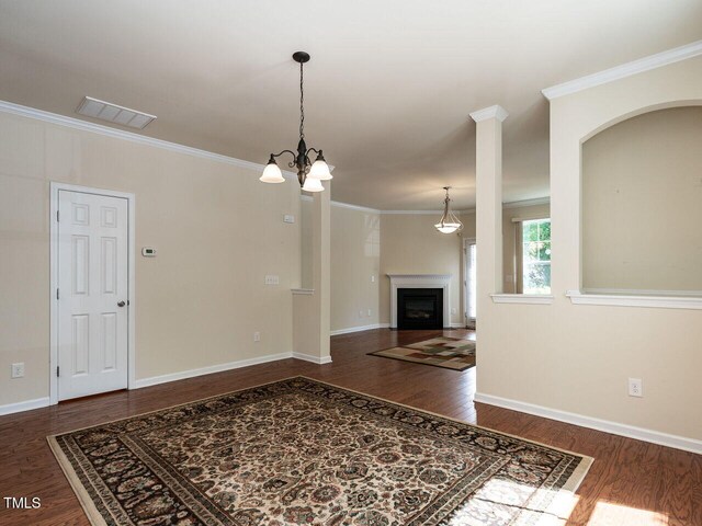 unfurnished living room with wood finished floors, ornamental molding, a fireplace, baseboards, and arched walkways