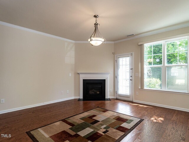 unfurnished living room with dark wood-style floors, crown molding, a fireplace with flush hearth, and baseboards