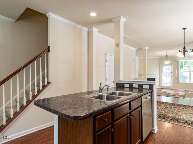 kitchen with a sink, dishwasher, dark countertops, ornamental molding, and dark wood-style flooring