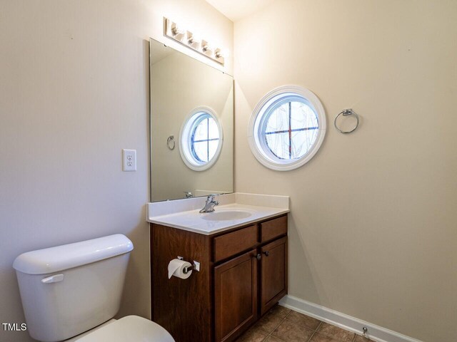 half bath with toilet, vanity, tile patterned flooring, and baseboards