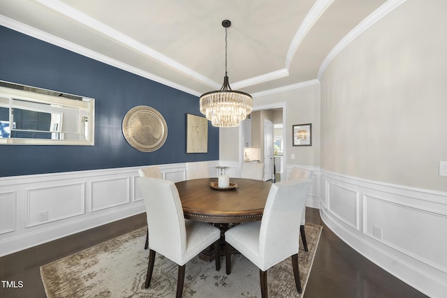 dining space with crown molding, an inviting chandelier, wainscoting, a raised ceiling, and dark wood-type flooring