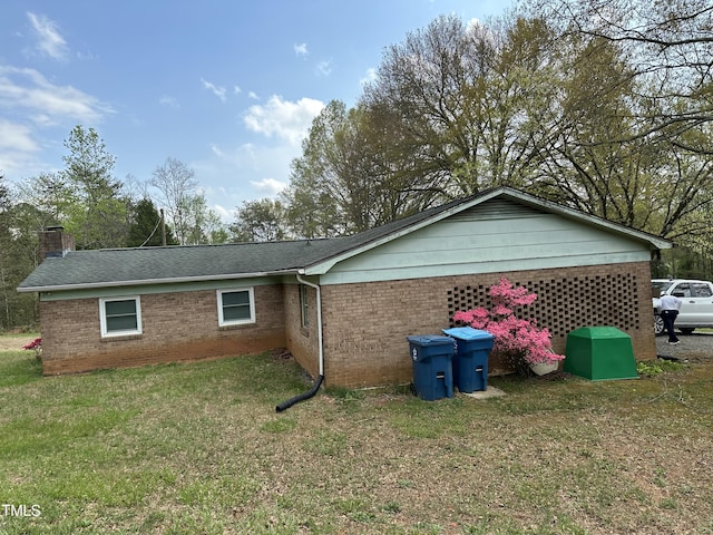 back of house with a chimney, a yard, and brick siding