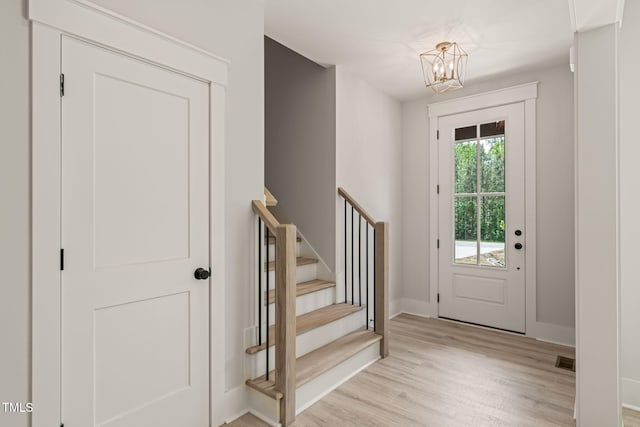 doorway to outside featuring an inviting chandelier, light wood-style floors, baseboards, visible vents, and stairway