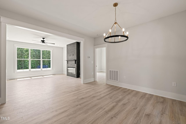 unfurnished living room featuring visible vents, a fireplace, baseboards, light wood finished floors, and ceiling fan with notable chandelier