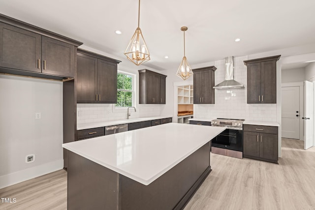 kitchen with wall chimney range hood, stainless steel appliances, dark brown cabinetry, and light wood-style flooring