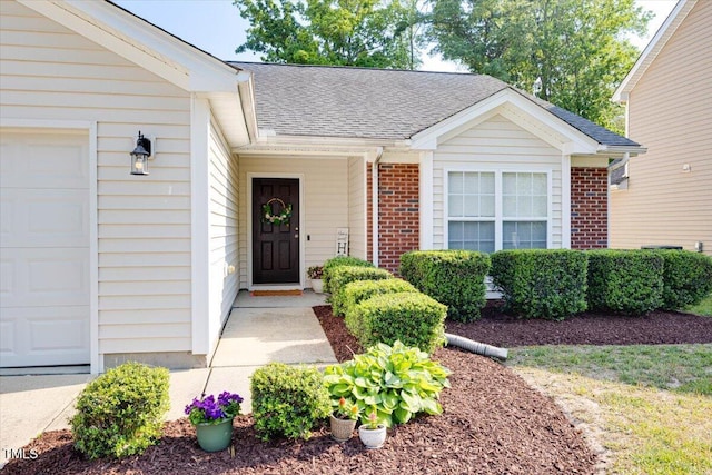 property entrance with brick siding, roof with shingles, and a garage