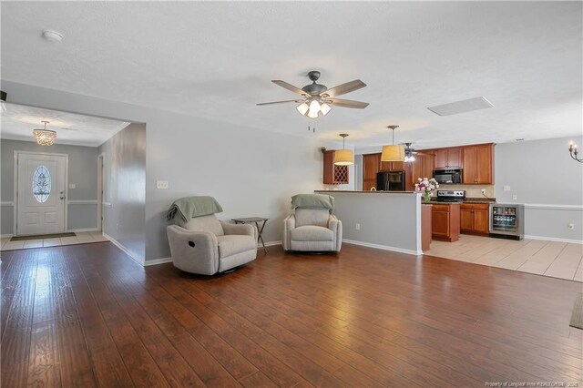 living area featuring wine cooler, baseboards, ceiling fan with notable chandelier, and light wood-style flooring