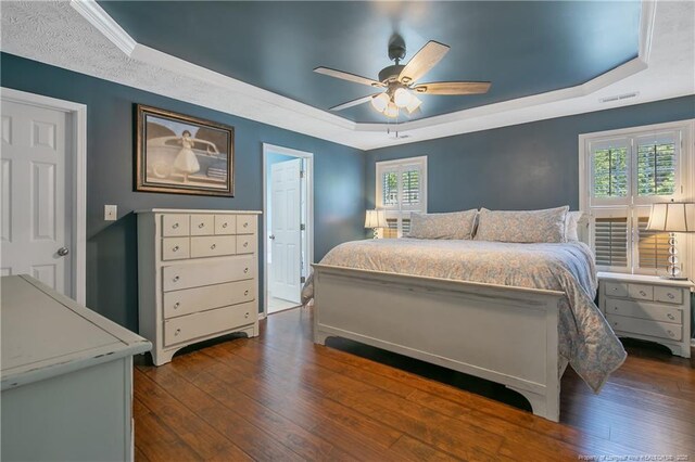 bedroom with ceiling fan, visible vents, a raised ceiling, dark wood-style floors, and ornamental molding