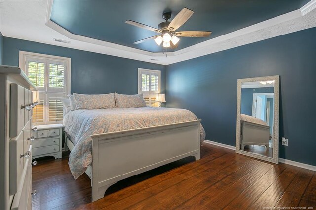 bedroom featuring visible vents, baseboards, dark wood-type flooring, and a tray ceiling