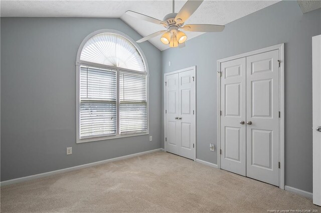 unfurnished bedroom featuring two closets, baseboards, lofted ceiling, and carpet