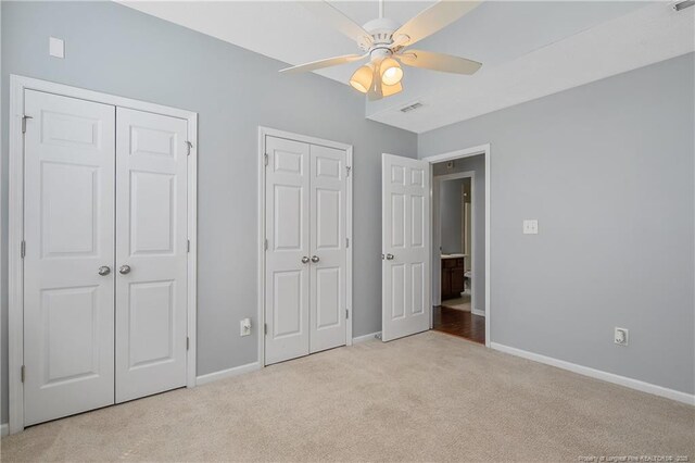unfurnished bedroom with visible vents, multiple closets, baseboards, a ceiling fan, and carpet