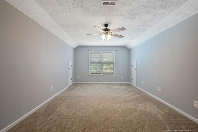 empty room with baseboards, light colored carpet, a textured ceiling, a ceiling fan, and vaulted ceiling