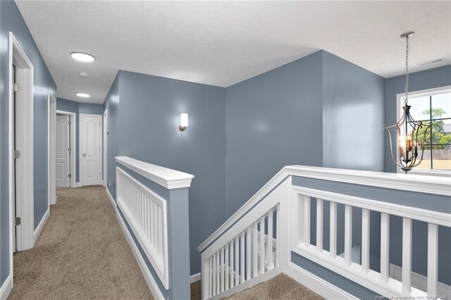 hall with baseboards, carpet flooring, a chandelier, and an upstairs landing